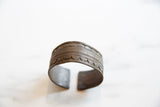 A collectible African bronze cuff bracelet shown from the side, detailing its aged patina and geometric engravings.