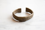 The curved, open profile of a collectible African bronze cuff bracelet with a time-softened patina.