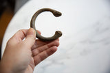 Hand holding an antique African copper alloy manilla cuff, showing textured patina.