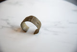 Angled view of the antique bronze cuff showing its open design and textured surface.