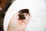 The substantial form and rich, aged patina of the antique bronze cuff held in hand.