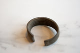 The distinct grooved stripes and curved shape of the antique bronze cuff bracelet.