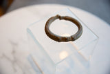 Angled view of an antique African bronze cuff with ridged texture and a deep, time-softened patina.