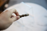 A hand holding the antique bronze cuff, showing the texture of its geometric segments.