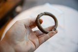 Antique African bronze cuff bracelet held in hand, displaying its scale and textured patina.