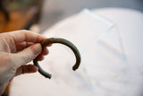 The dark, aged patina and curved C-shape of the antique African copper cuff.
