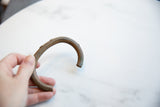 A hand holding the antique copper cuff bracelet, showing its scale and aged surface patina.