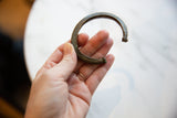 Hand holding antique African bronze cuff bracelet, highlighting intricate textured ends.