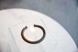 The solid, open C-shape of an antique African bronze cuff with a dark, textured patina.