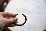 Antique African bronze cuff held to display its open C-shape and scale.