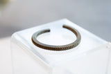 Profile view of the antique bronze cuff showing its open shape and striped outer edge.