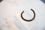 The circular form and ridged texture of an antique bronze African cuff, viewed from an angle.