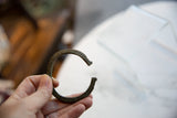 Hand holding the antique bronze bracelet, showing its scale and striped craftsmanship.