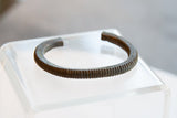 The handcrafted, ribbed texture and open cuff shape of an antique African bronze bracelet.