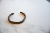 Angled view of an antique bronze African cuff showing its open shape and striped texture.