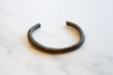 Antique bronze cuff bracelet seen in profile, showing its striped texture and aged patina.