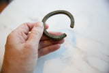 Antique African bronze cuff held to show scale, revealing its striped texture and dark patina.