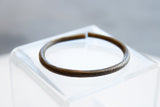 Close view of an antique bronze bracelet highlighting its dark patina and faded etched markings.