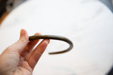 The curved shape and dark, textured patina of the vintage bronze artifact.