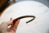 A hand holds the curved bronze artifact, highlighting its time-worn patina.