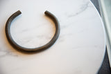 Vintage African bronze artifact displaying its open C-shape and handmade, textured surface.