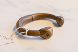 Close-up profile of an antique copper cuff, showing the time-softened patina and etched end.