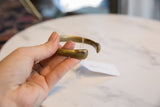 A hand holds the antique bronze cuff, showing the smooth patina on its rounded end.