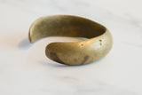 The substantial, curved body of the antique bronze cuff with its aged golden patina.