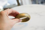 A hand holds an antique bronze cuff, showing its substantial size and golden patina.