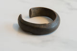 Side profile of an antique African currency bracelet highlighting its thick form and dark patina.