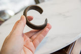 Antique copper alloy bracelet held in hand, showing its C-shape and scale.