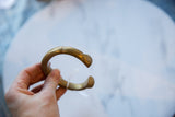 Antique African bronze cuff held to show its substantial C-shape and golden patina.