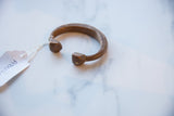 The thick, rounded ends and open cuff shape of an antique copper alloy bracelet.