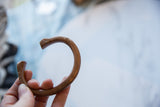 Antique African copper snake bracelet held to show its open cuff shape and scale.