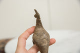 A hand holds the bronze Kori bustard bird, showing its textured back and scale.
