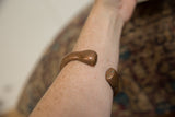 Antique copper snake bracelet with a time-softened patina worn on the forearm.
