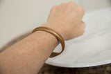Smooth antique copper snake bracelet with a warm patina, shown worn on a wrist.