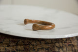 Angled view of the antique African copper bracelet's C-shaped form and time-softened patina.