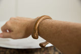 The sculptural form of an antique copper snake bracelet worn on the forearm.