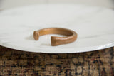 Hand-hammered texture and aged patina on the flared terminal of an antique copper bracelet.