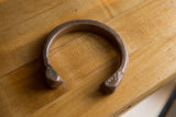 The curved shape and hand-etched surface of the antique African copper snake cuff.