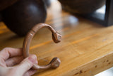 Hand holding the antique copper snake cuff, highlighting its warm patina and crafted ends.