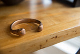 Angled view of the antique copper cuff's smooth, rounded terminals and hand-formed shape.