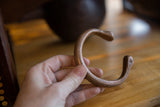 Hand holding an antique copper snake cuff to show its scale and warm patina.