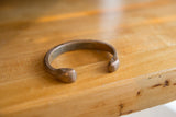 Side profile of an antique African copper bracelet showing its open cuff and snake heads.