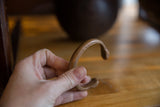 A hand holding the antique African copper bracelet to show its scale and incised markings.