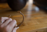 Stylized snake head terminal with stamped patterns on an antique copper cuff bracelet.
