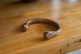 The aged patina and hand-faceted detail on the terminal of an antique copper snake cuff.