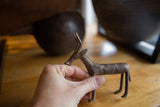 Hand holding vintage African bronze antelope, showcasing its unique incised body texture.