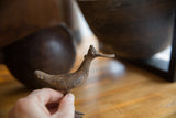 A hand holds the vintage African bronze bird, showing its textured handmade finish.